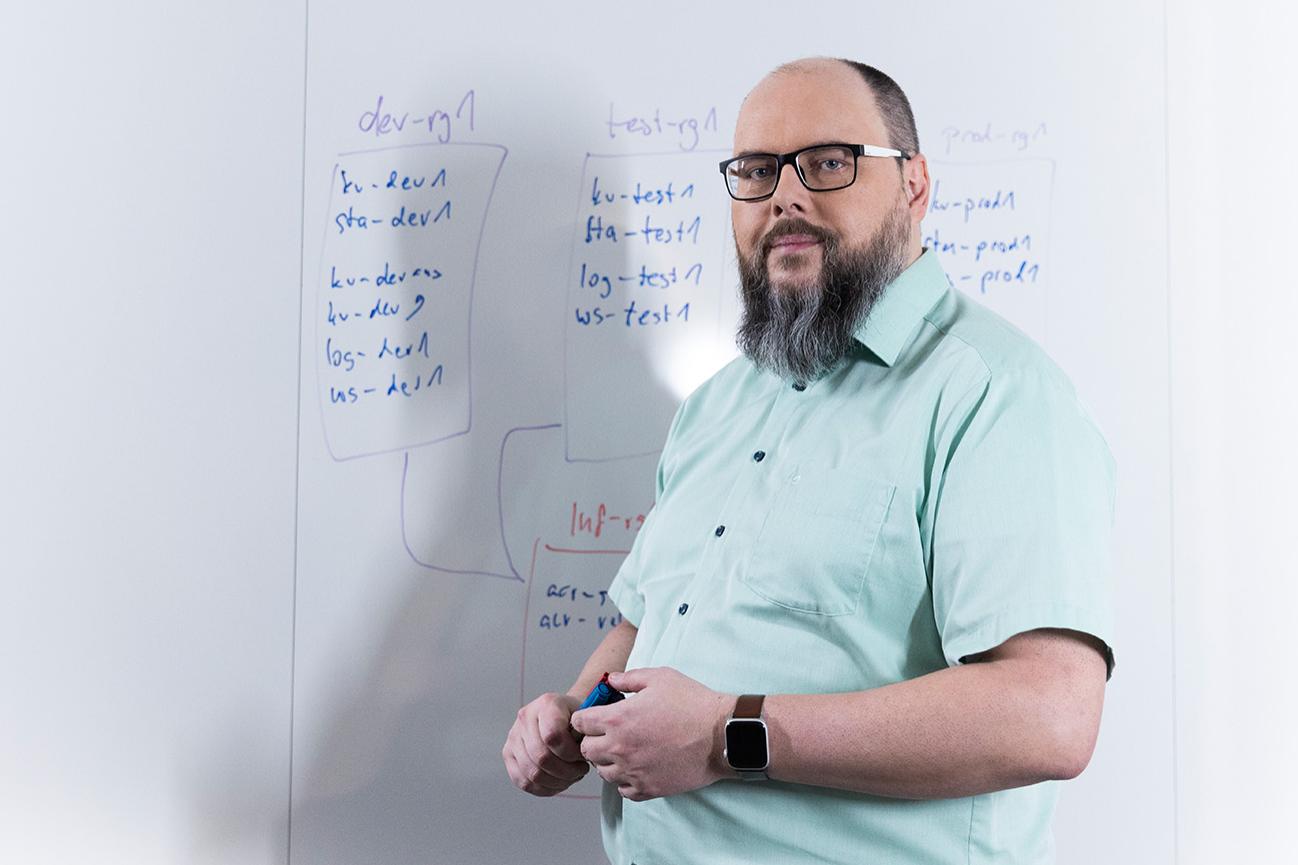 Sven steht vor einem Whiteboard seinem Kollegen gegenüber und erklärt gestikulierend den Inhalt der Notizen darauf