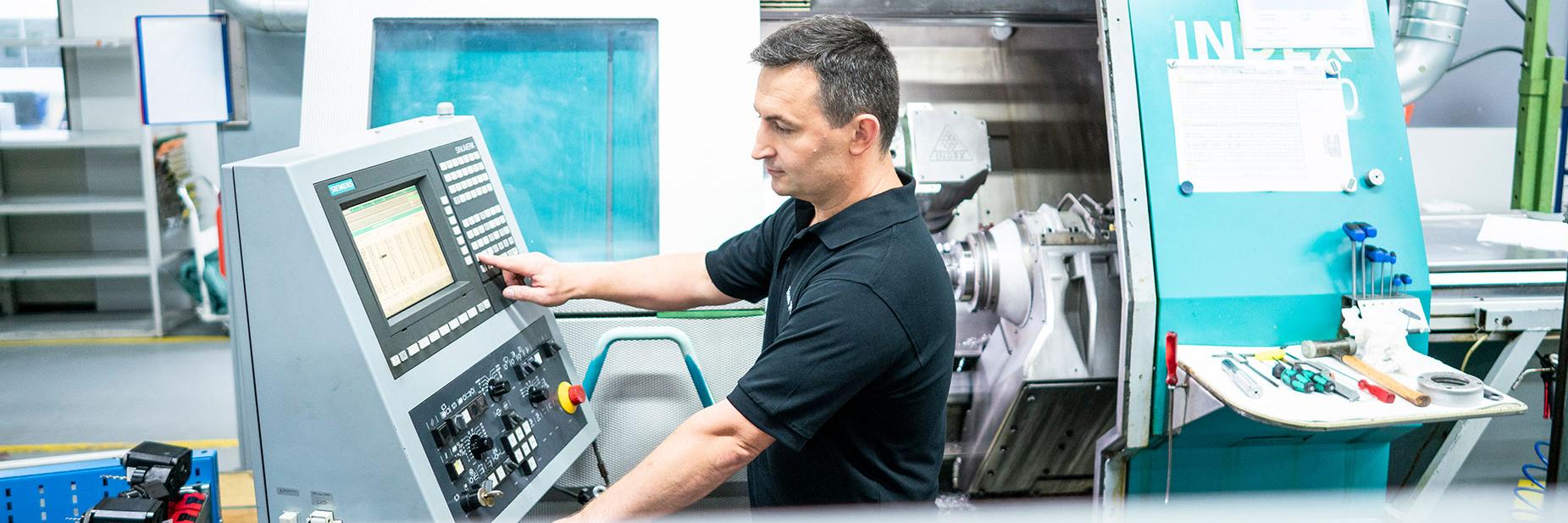 Waldemar stands next to a control panel and operates a metal processing machine.