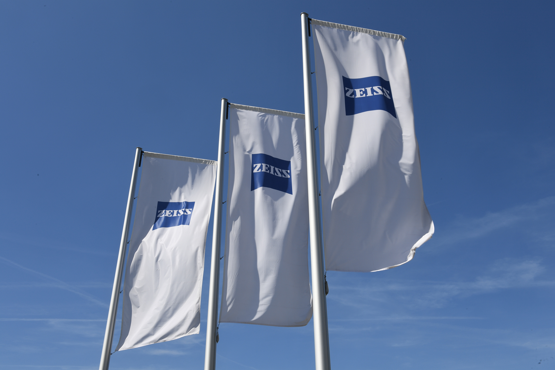 Three white flags with ZEISS logo in front of a blue sky