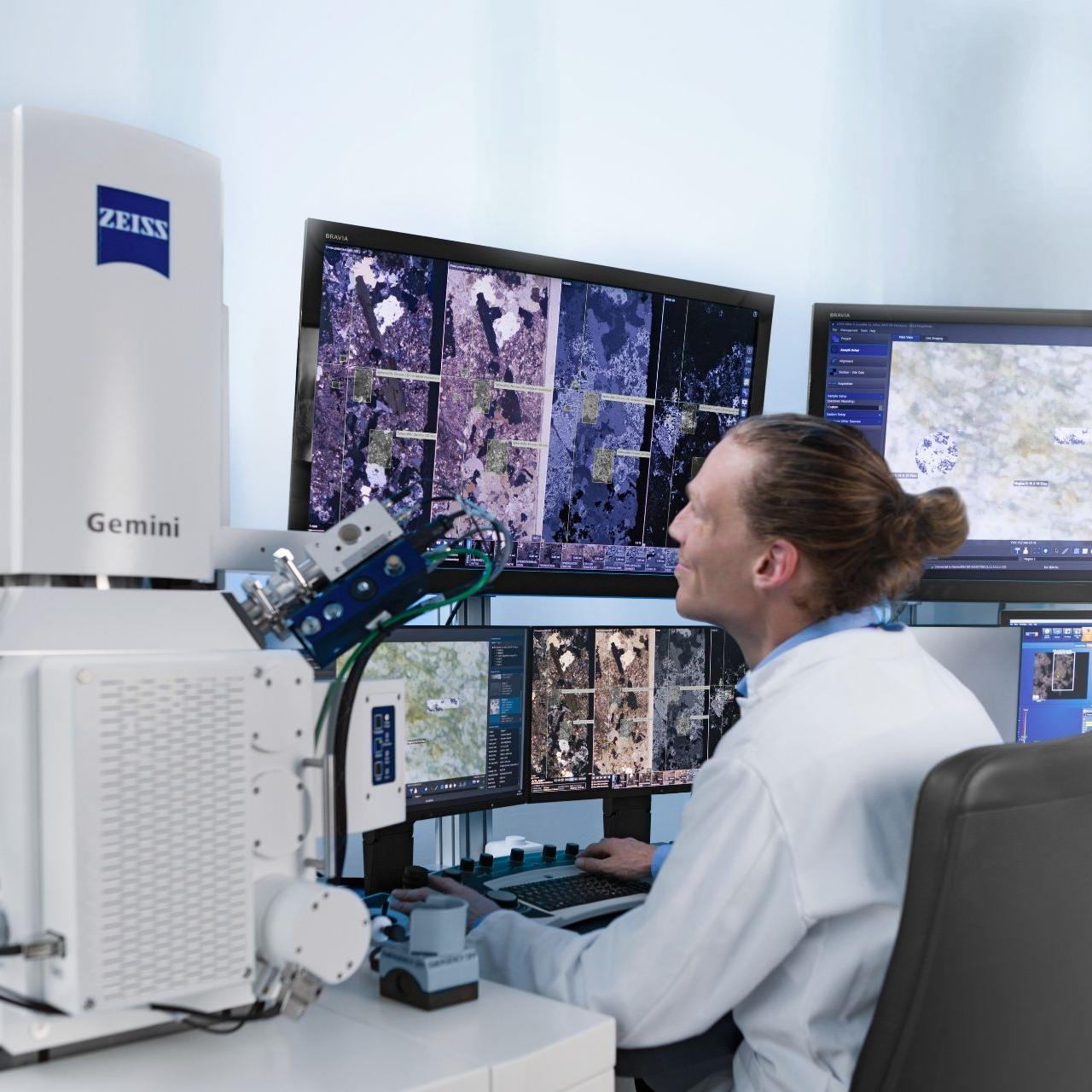Researcher working at a workstation with a ZEISS Gemini microscope, surrounded by multiple screens displaying high-resolution scientific imaging data.